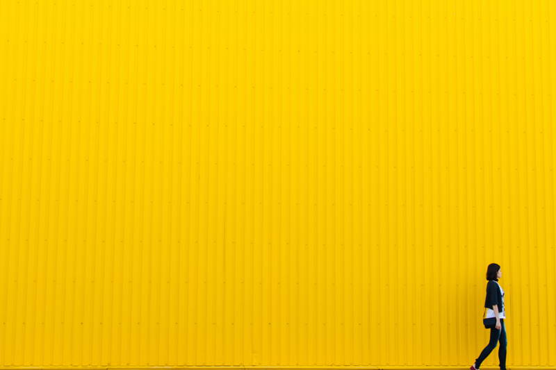 Woman walking in front of a yellow wall