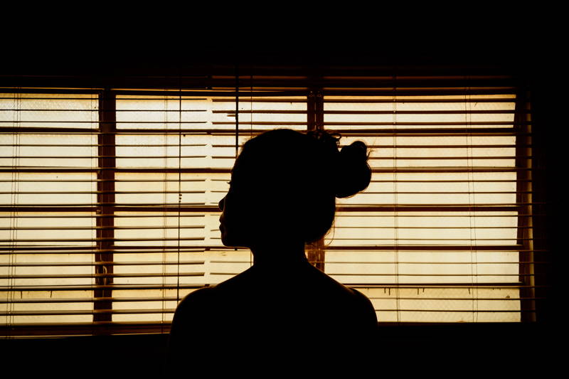 Silhouette of woman sitting in the dark recovering from hustle culture