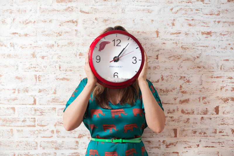 Woman holding a clock in front of her face to indicate a fast-paced work environment