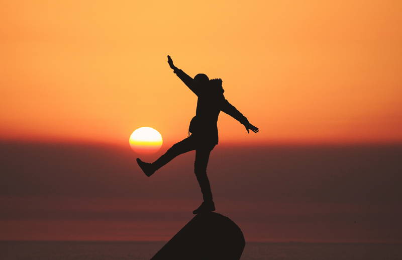 Woman balancing on a rock at sunset