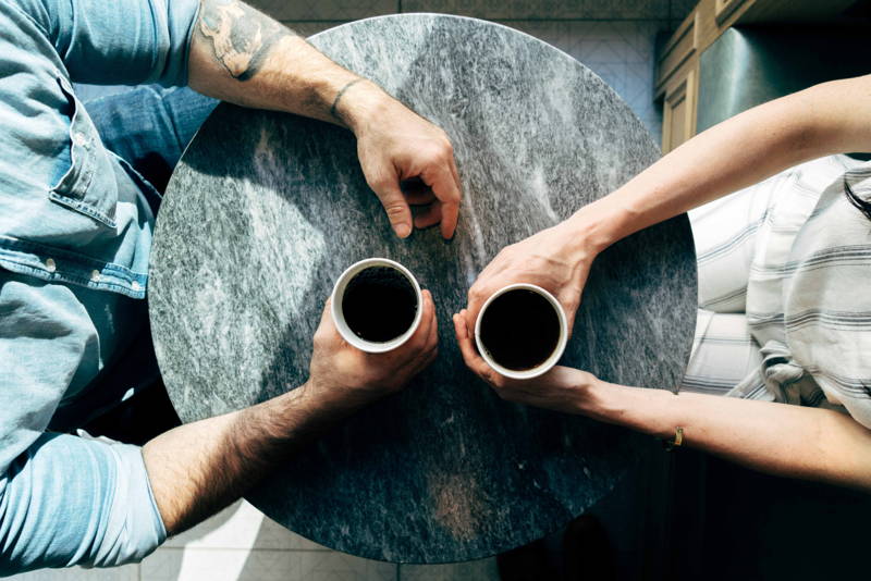 Two coffee cups on table held by employee and boss negotiating salary